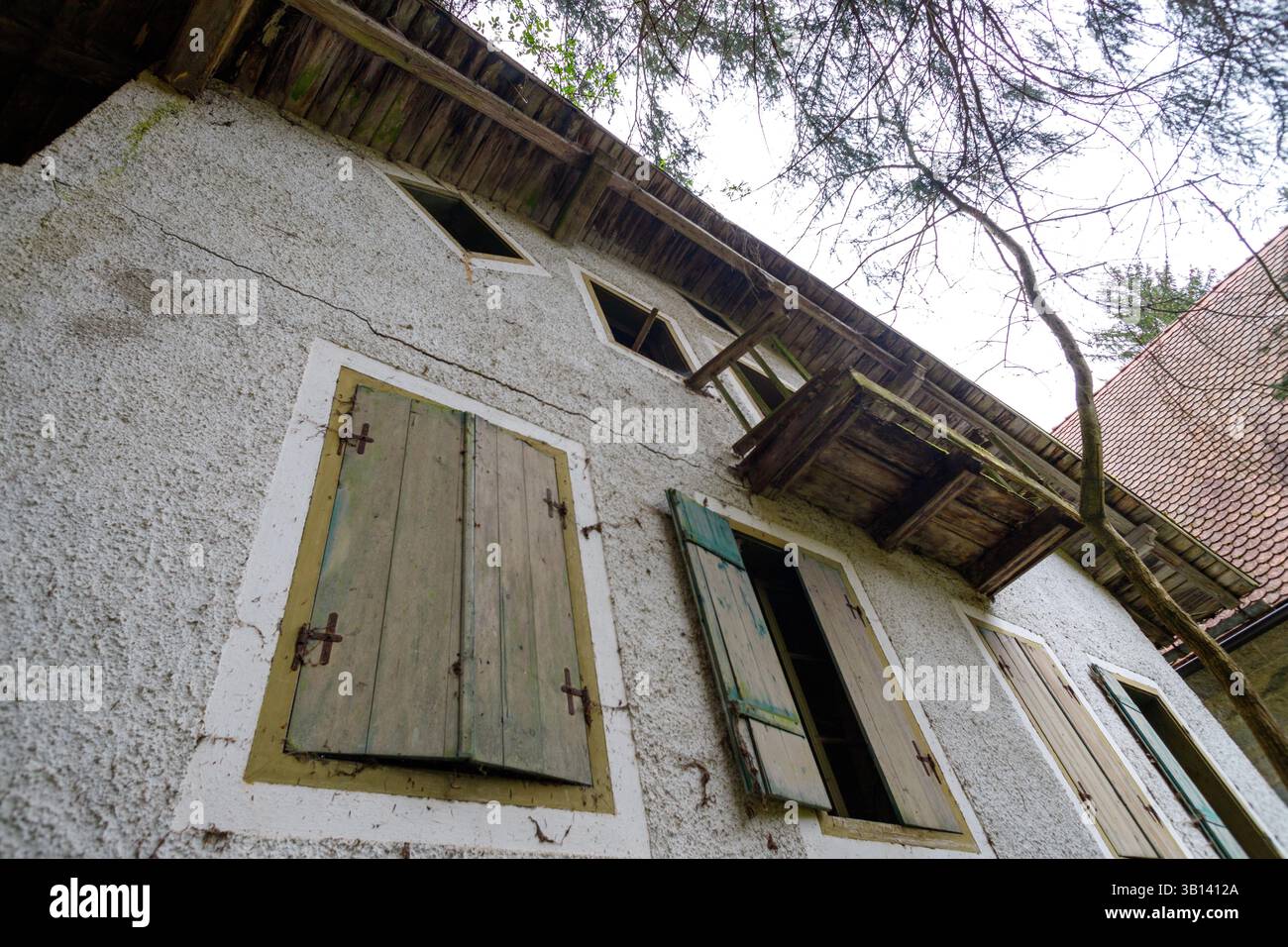 Bad Illstern, italia, posto perso. Inquadratura ad angolo basso di un edificio a due piani con persiane di legno, un piccolo balcone e danni al tetto, vista agai Foto Stock