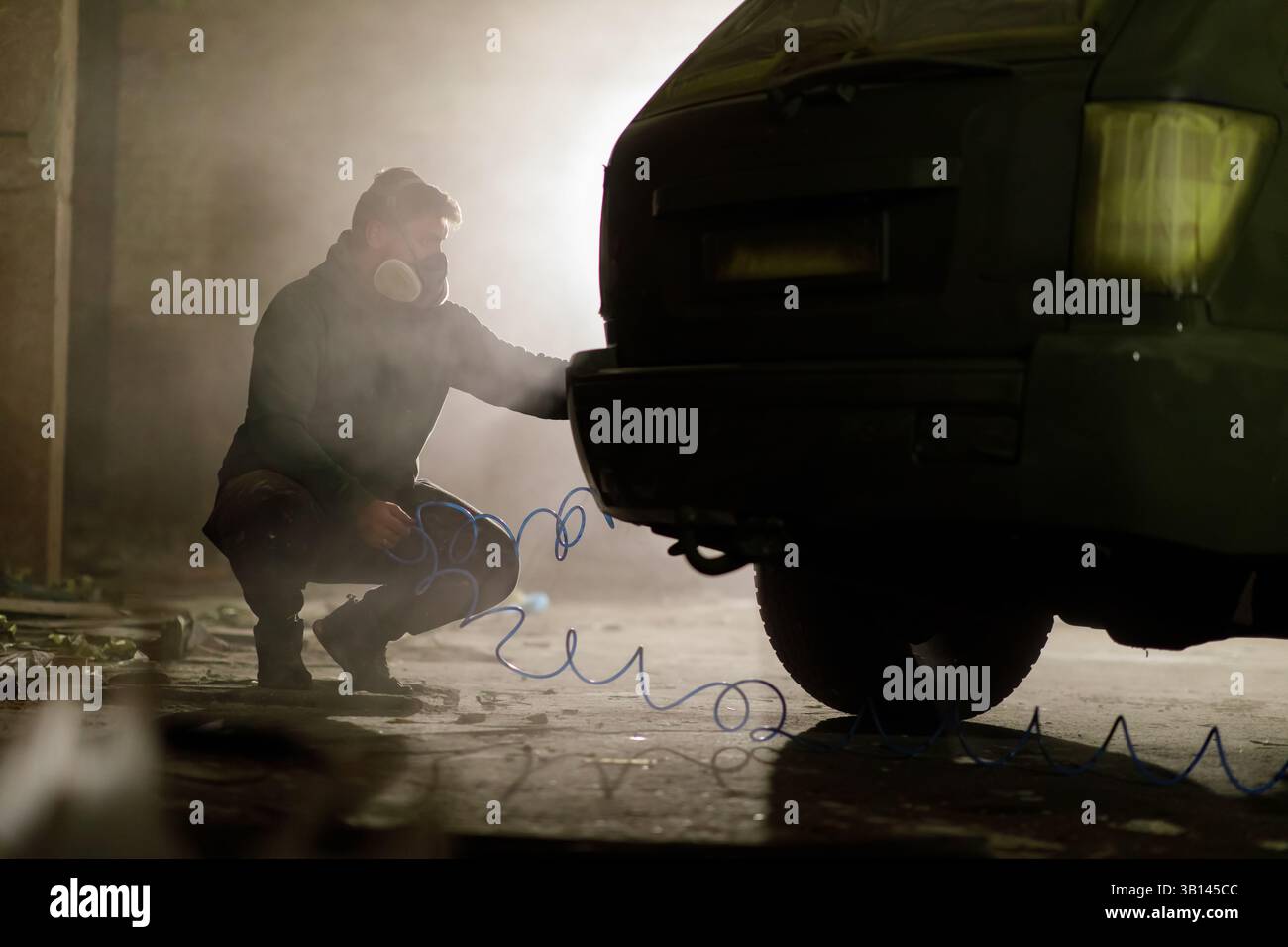 Un meccanico si concentra sulla riparazione della parte posteriore di un veicolo in un garage scarsamente illuminato. L'atmosfera e' piena di polvere e il bagliore delle attrezzature circostanti Foto Stock
