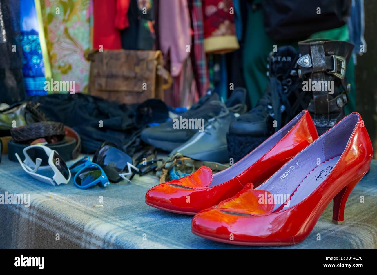 Scarpe rosse lucide con tacco alto in mostra presso uno stand del mercato delle pulci di Berlino, circondate da abiti e accessori vintage. Foto Stock