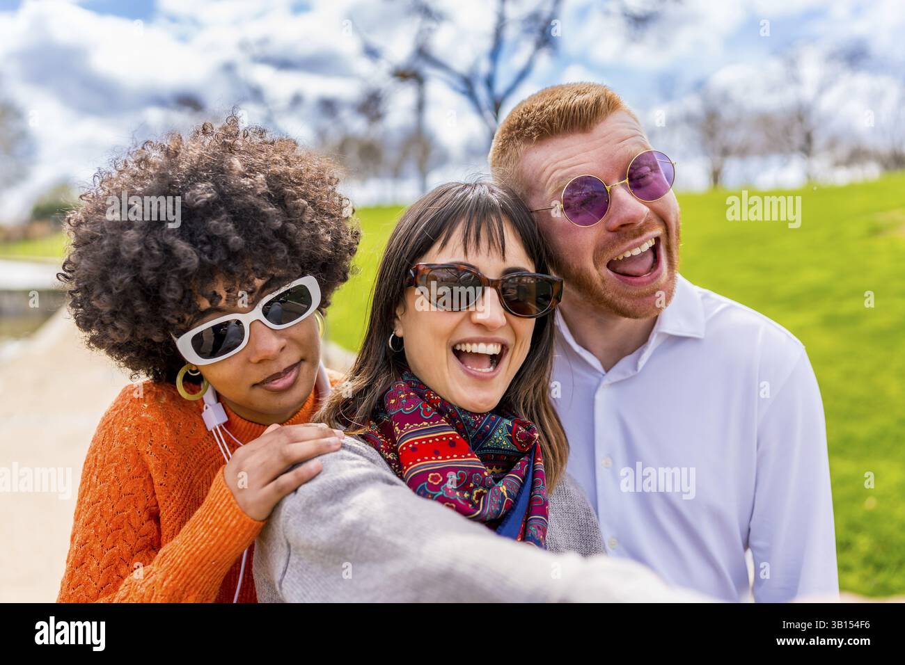 Tre allegri amici multietnici si stanno facendo un selfie in un parco, ridendo e godendosi una bella giornata di sole insieme Foto Stock