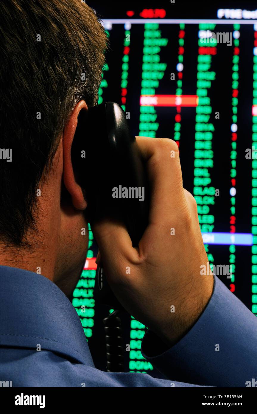 Agente di borsa che utilizza un telefono davanti a una visualizzazione dei prezzi del mercato azionario Foto Stock