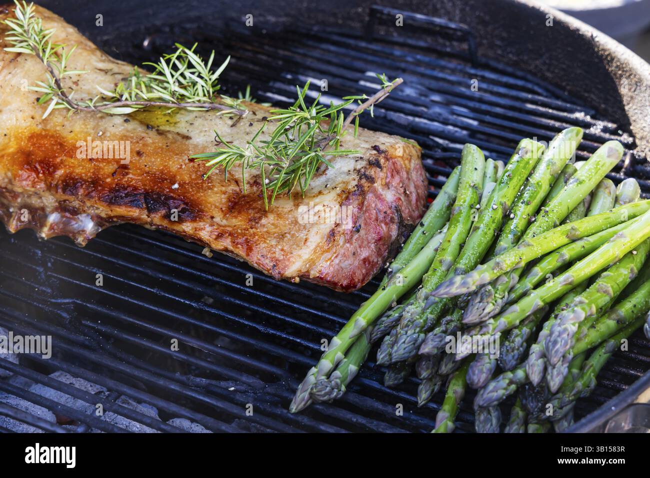 Barbecue con arrosto di Pasqua. Griglia di agnello e asparagi verdi grigliati su un bollitore per barbecue all'aperto. Carne e verdure vegetariane. Baden-Wuerttemberg Foto Stock