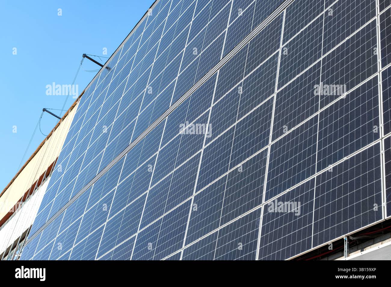 Montaggio di una vasta gamma di pannelli solari sul lato di un edificio. Verricelli, strutture di supporto e cablaggio elettrico sono visibili. Foto Stock