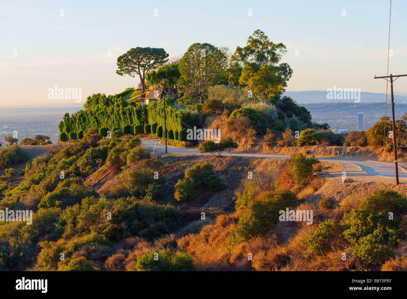 Vista panoramica da un sentiero escursionistico al Runyon Canyon Park, con vegetazione lussureggiante, sentieri tortuosi e l'ampio skyline di Los Angeles durante il Golden hou Foto Stock
