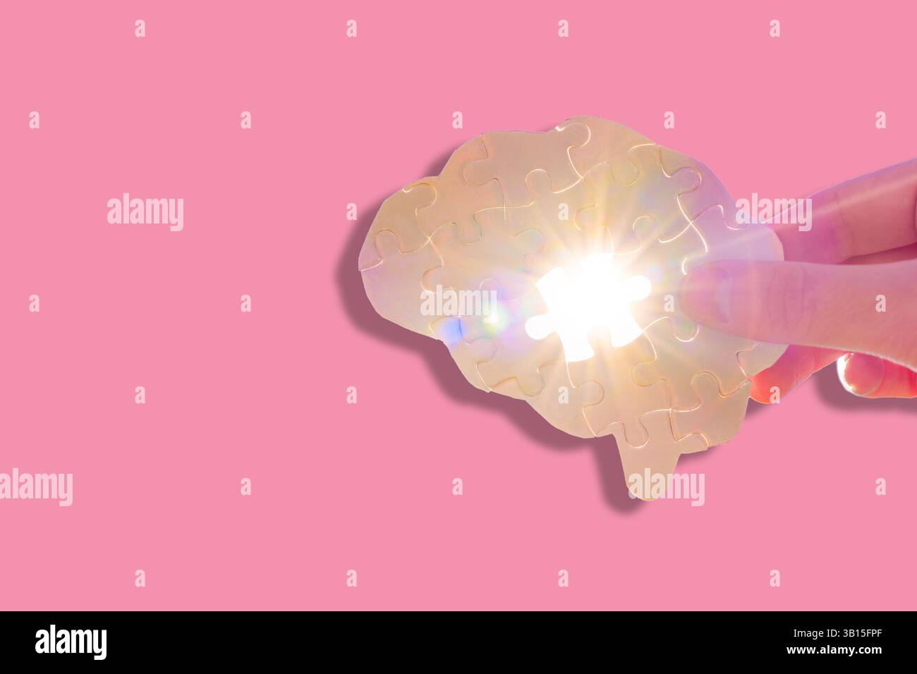 Primo piano di una mano che regge un pezzo di puzzle a forma di cervello su uno sfondo rosa, simboleggiando lo studio delle funzioni della mente nella neuroscienza. Foto Stock