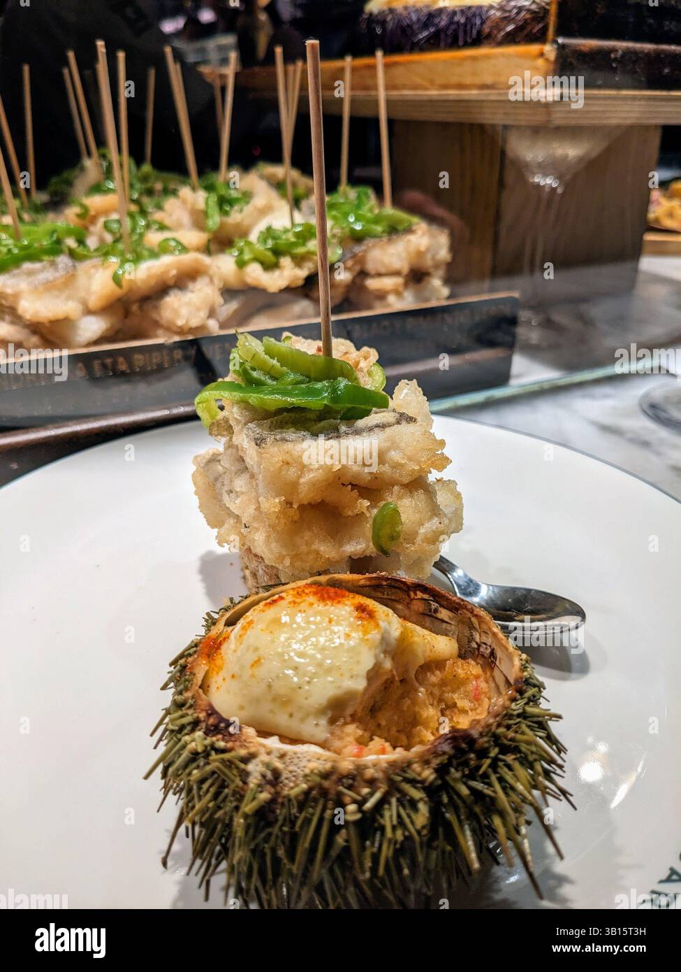 Un piatto presenta piatti gourmet unici che includono pesce fritto con peperoni verdi e ricci di mare. Delizia culinaria in un ambiente raffinato. Foto Stock