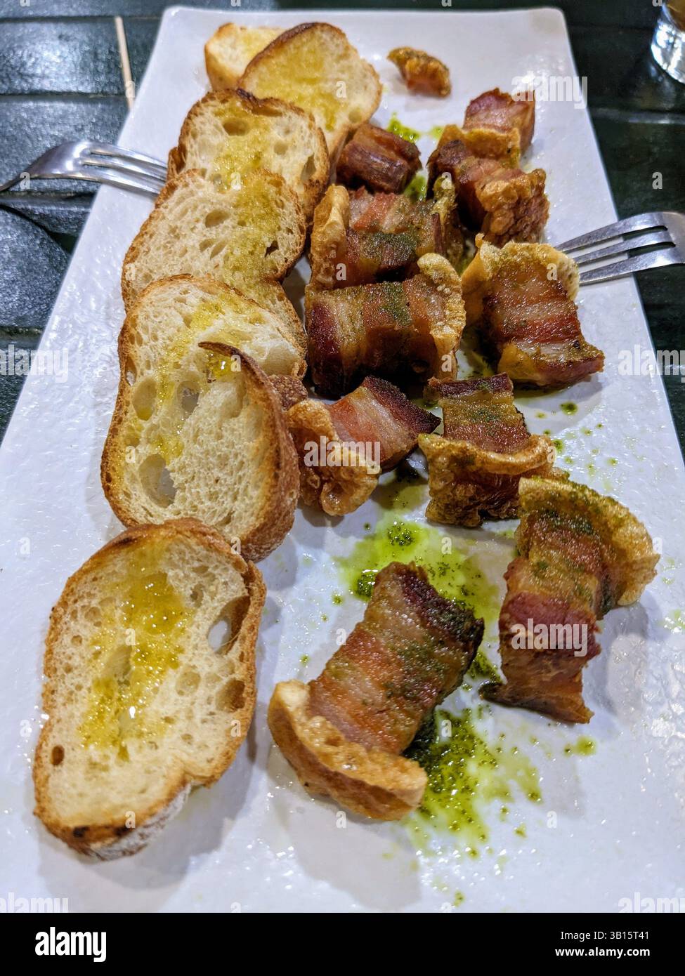 Un piatto di pancia di maiale croccante e pane tostato con olio sgusciato, perfetto da condividere. Il piatto è servito su un piatto bianco con salsa verde. Foto Stock