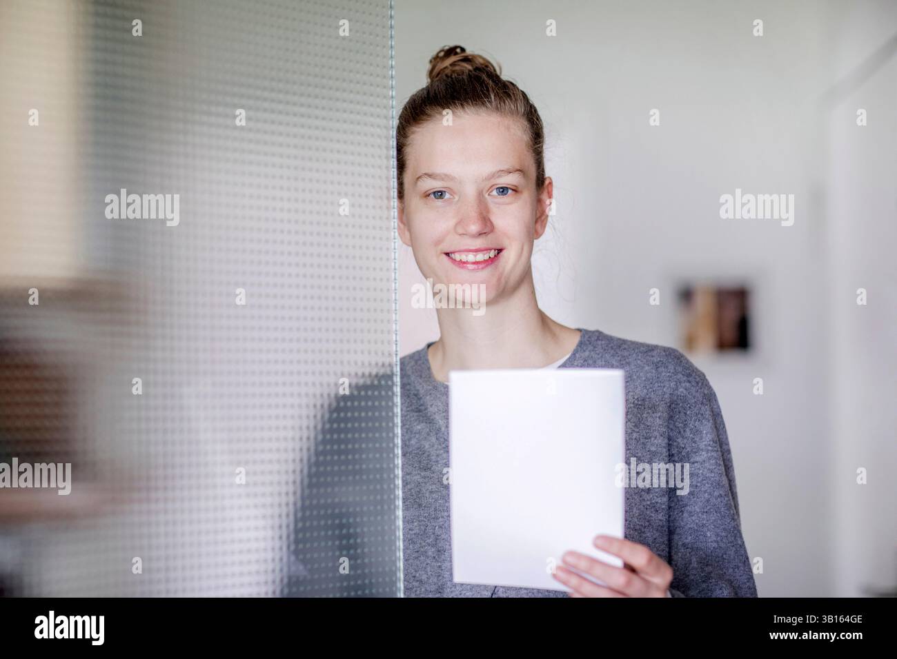 Giovane donna in piedi dietro una porta di vetro Foto Stock
