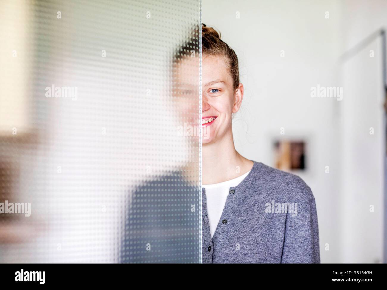 Giovane donna in piedi dietro una porta di vetro all'interno Foto Stock