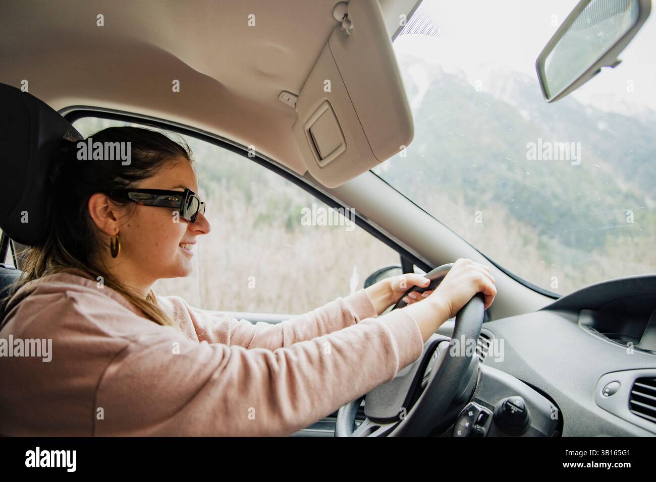 Donna sorridente che guida un'auto attraverso una strada di montagna Foto Stock
