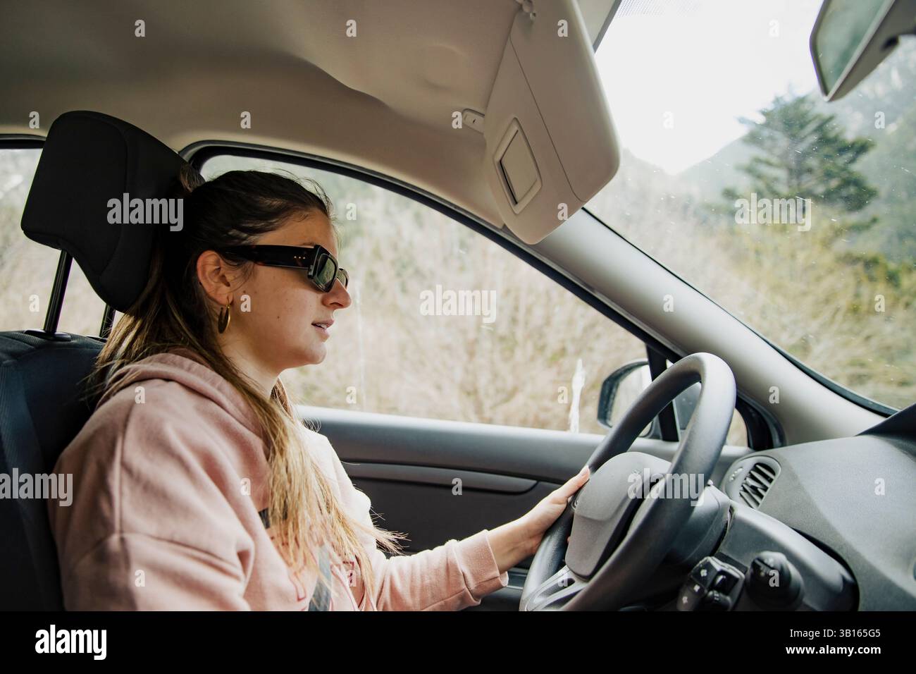 Donna sorridente che guida un'auto attraverso una strada di montagna Foto Stock