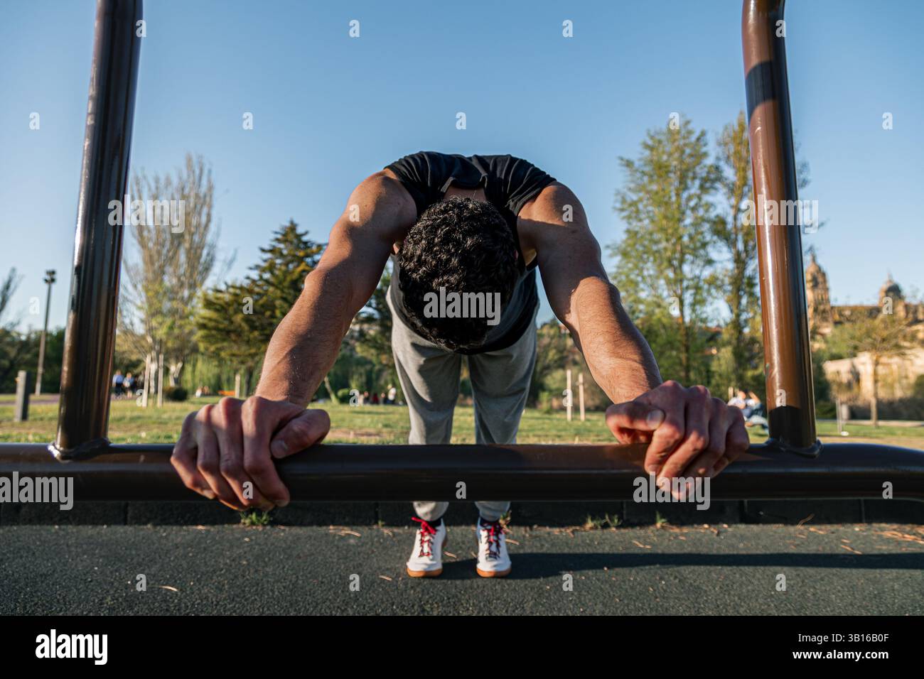 L'uomo che esegue il Dynamic Bar stretch o la calistetica si affida alle attrezzature per il fitness all'aperto, mettendo in risalto la tensione della parte superiore del corpo, la concentrazione e la disciplina fisica Foto Stock