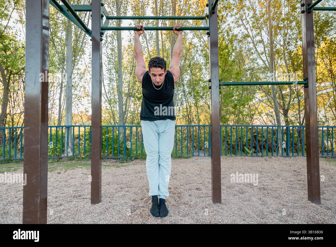 Uomo atletico appeso ancora sulla barra di calistenica nella pelle il movimento Cat, che mostra forza di presa e prontezza del corpo all'aperto Foto Stock