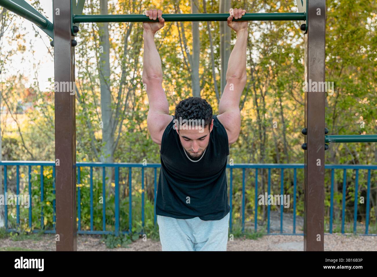Primo piano di un atleta appeso al fitness bar all'aperto, che sottolinea la forza del braccio, la stabilità e il coinvolgimento nella parte superiore del corpo durante la routine di allenamento con il peso corporeo Foto Stock