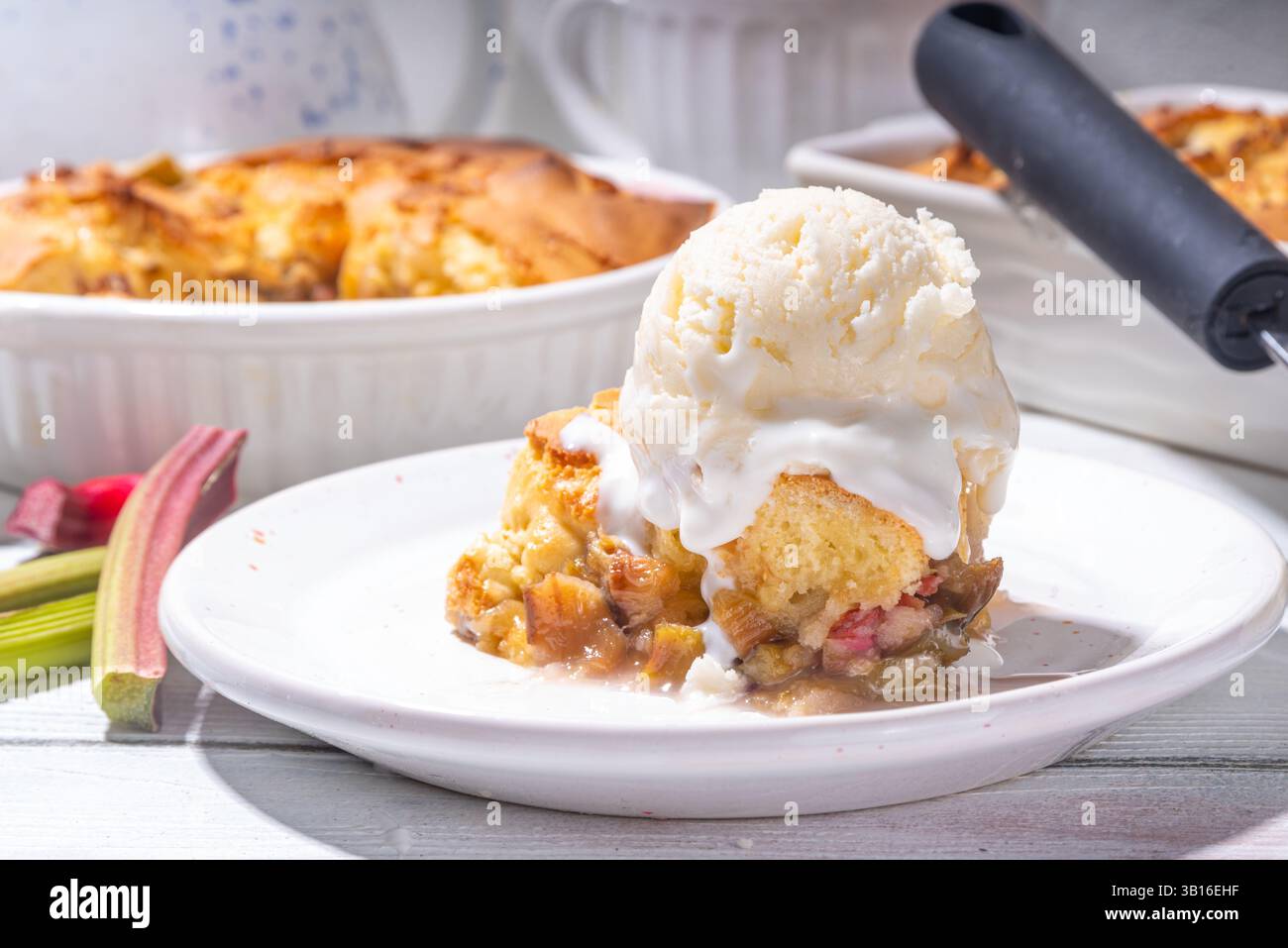 Torta di acciottolato dolce al rabarbaro, pan di Spagna fatto in casa con rabarbaro zuccherato e fragola, servito con palla di gelato alla vaniglia, su soleggiato k di legno bianco Foto Stock