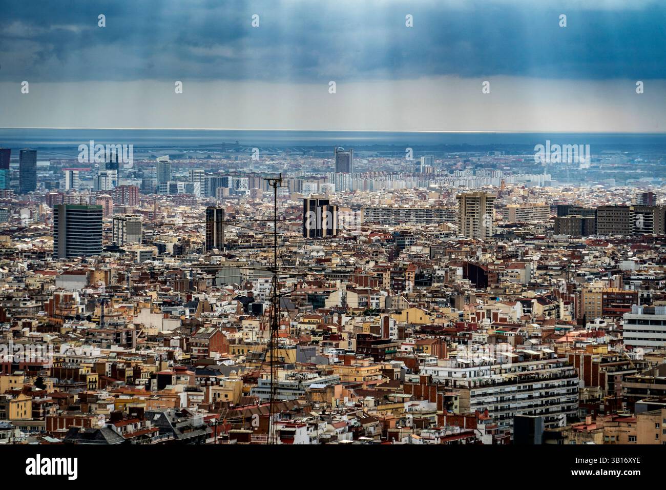 Una vista panoramica di un vasto paesaggio urbano sotto un cielo nuvoloso, con raggi di luce del sole che si infrangono tra le nuvole. Il paesaggio urbano presenta un mix di Foto Stock