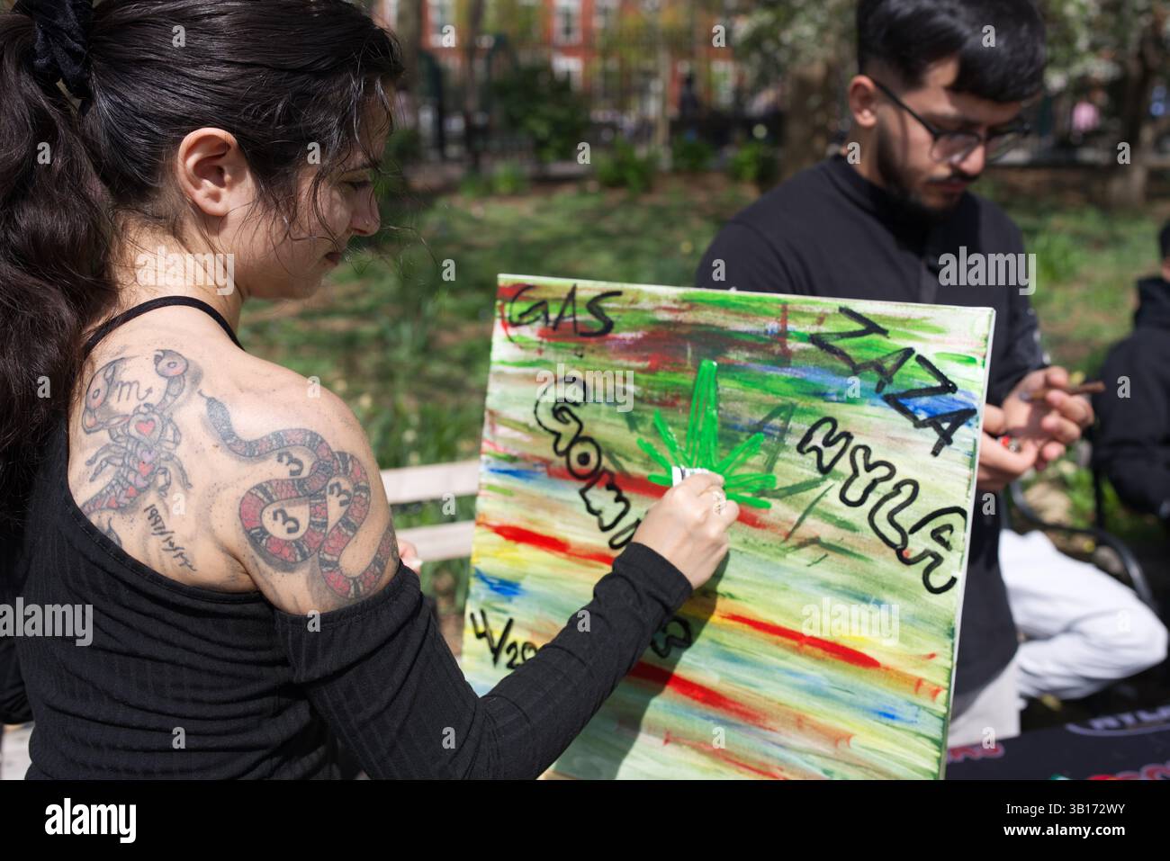 Una donna con uno scorpione e un tatuaggio di serpente dipinge una foglia di cannabis su una tela colorata con scritte in stile graffiti, tra cui "Zaza" e "gas". Un altro Foto Stock Una donna con uno scorpione e un tatuaggio di serpente dipinge una foglia di cannabis su una tela colorata con scritte in stile graffiti, tra cui "Zaza" e "gas". Un altro Foto Stock