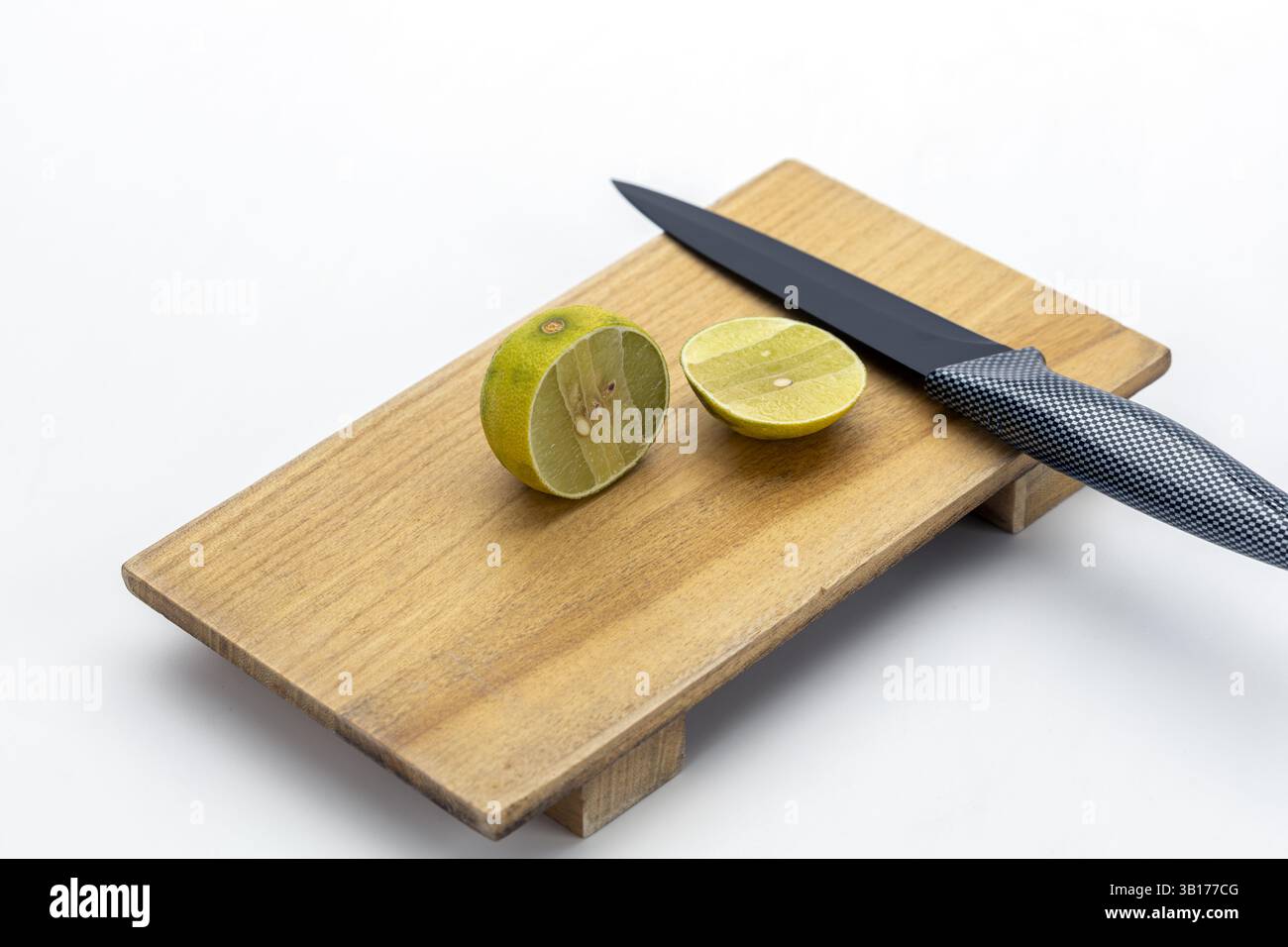 Sapori aspri nel cibo thailandese: Spicchi di lime posti accanto a un coltello da cucina nero su un tagliere di legno che esaltano il sapore e la freschezza del lime Foto Stock