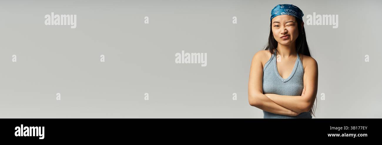 Una giovane donna asiatica sicura di sé in un outfit elegante si staglia con le braccia incrociate, trasudando fascino. Foto Stock