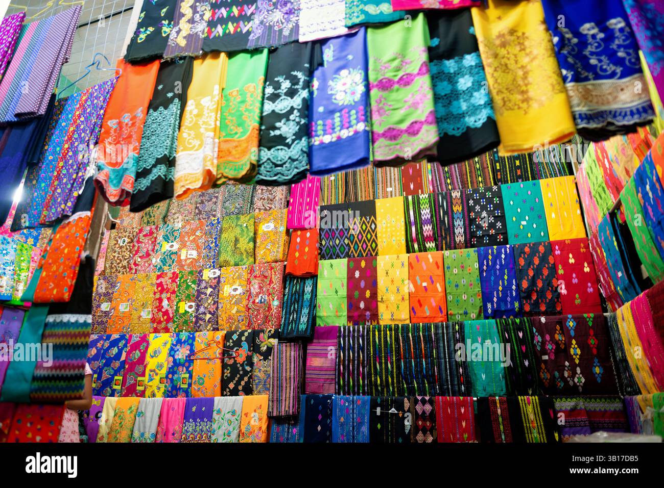 Betel Leaves display Zegyo Market Mandalay Myanmar // MANDALAY, Myanmar — le foglie di Betel sono impilate con cura e disposte in un modello circolare presso la bancarella di un fornitore nel mercato di Zegyo. Queste fresche foglie verdi del vitigno Piper betle servono da involucro per il liquido di betel (noto localmente come kun-ya), un leggero stimolante ampiamente consumato in Myanmar. La meticolosa disposizione riflette sia considerazioni pratiche per mantenere la freschezza che i valori estetici tradizionali negli schermi di mercato. I venditori di betel in genere vendono non solo le foglie, ma anche altri ingredienti necessari per la preparazione del liquido, Foto Stock