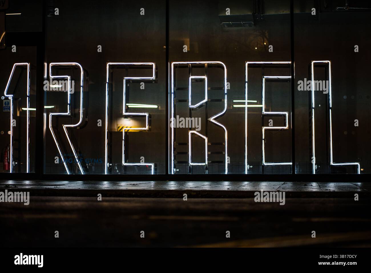 Il grande cartello al neon che indica "REBEL" si illumina di notte dietro una finestra, creando una suggestiva scena urbana. Foto Stock