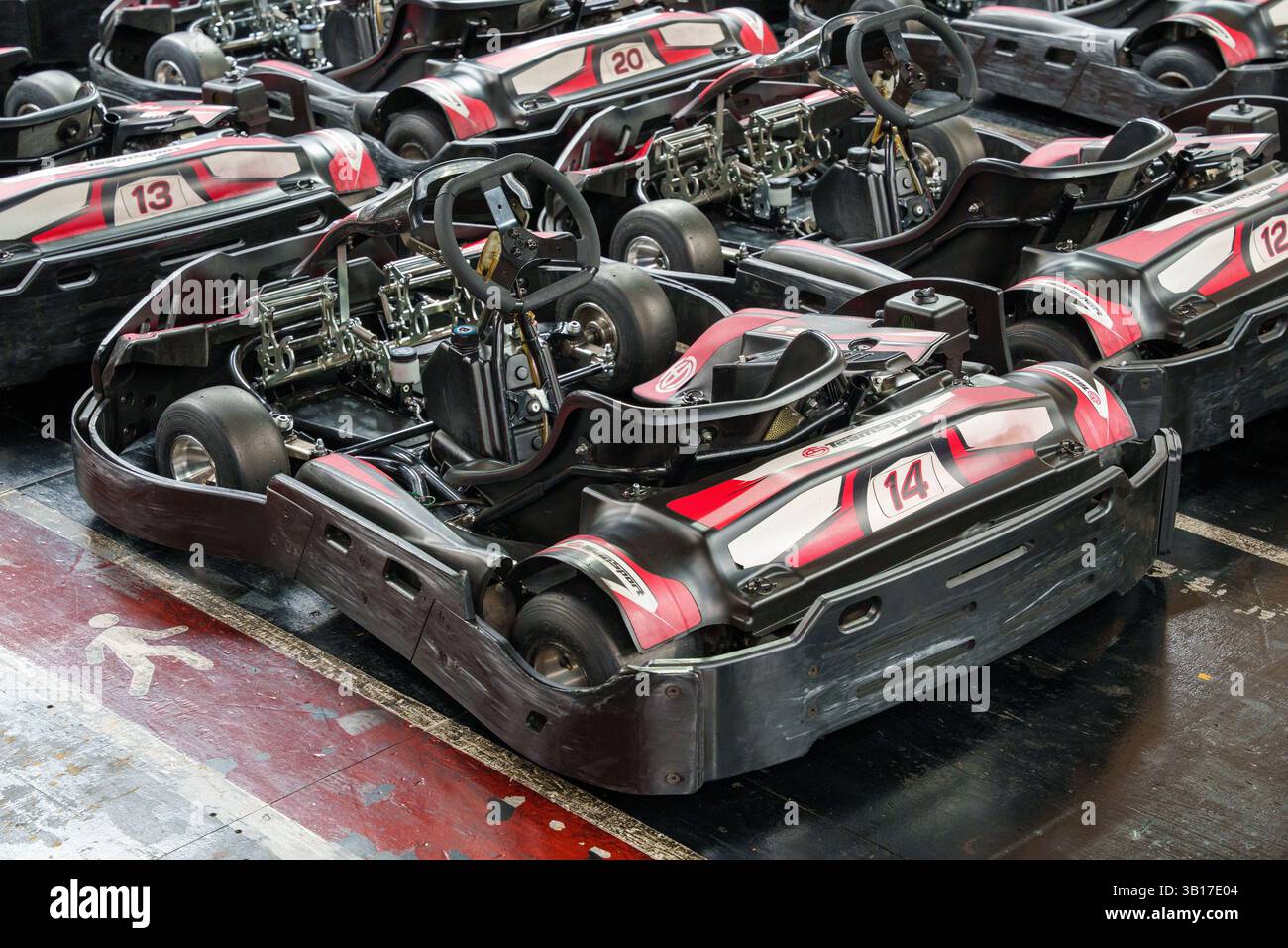 Una flotta di go-kart rossi e neri attende i piloti, pronti per l'azione su una pista di karting al coperto. Foto Stock