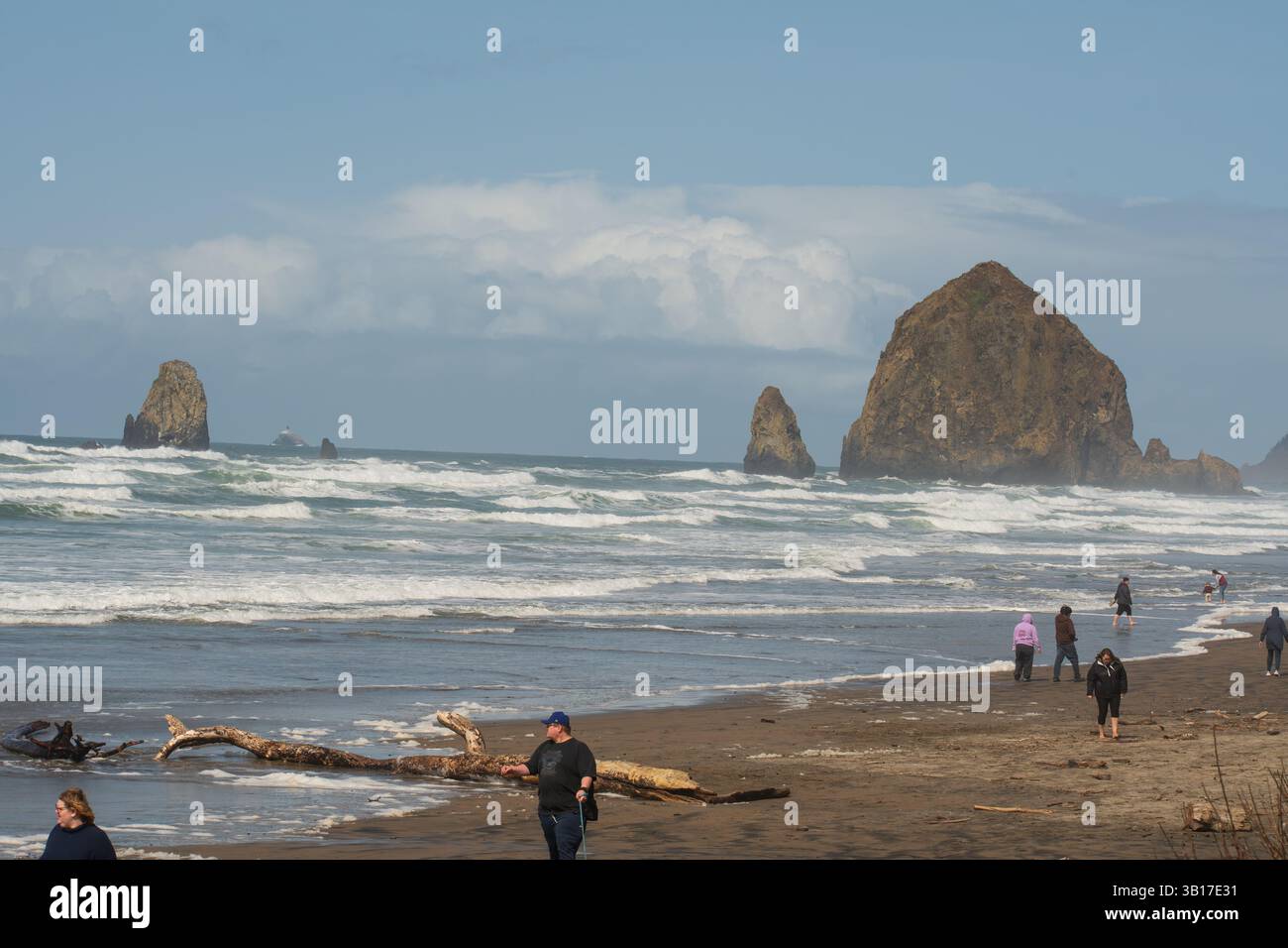 CANNON BEACH, OREGON, USA - 12 aprile 2025: I visitatori camminano lungo le spiagge sabbiose di Cannon Beach sotto un cielo nuvoloso, con l'iconica Haystack Rock in piedi. Foto Stock