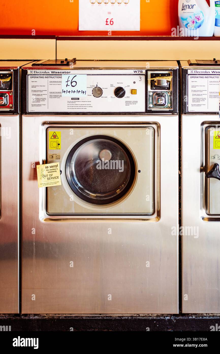 Una lavatrice Wascator W75 Electrolux fuori servizio in lavanderia automatica, al prezzo di £6, con parete arancione e detergente Lenor sullo sfondo. Foto Stock