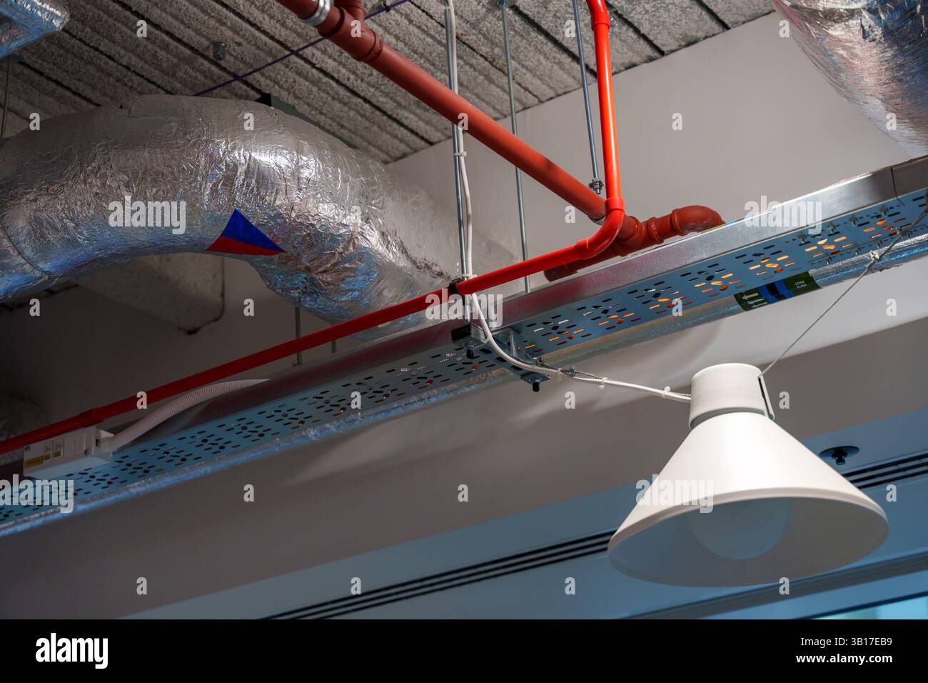 Moderna infrastruttura a soffitto per uffici con tubi a vista, condotti, cablaggi e lampada a sospensione minimalista. Foto Stock