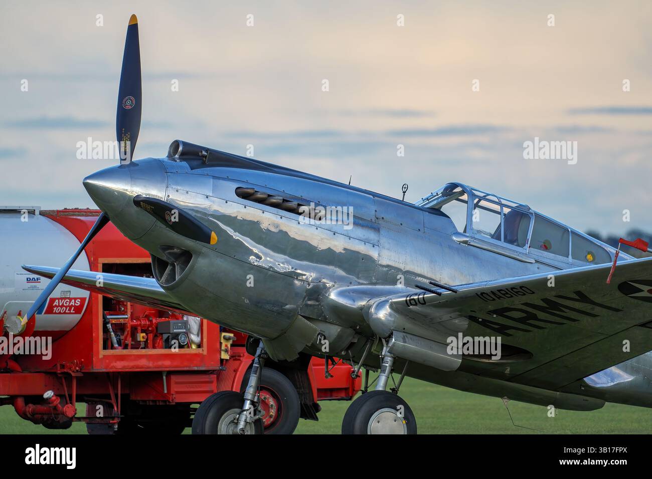 Uno scintillante Curtiss P-40 Warhawk, un classico aereo da combattimento americano della seconda guerra mondiale, attende il decollo su un campo d'aviazione erboso sotto un cielo soffice e nuvoloso a Duxford. Foto Stock