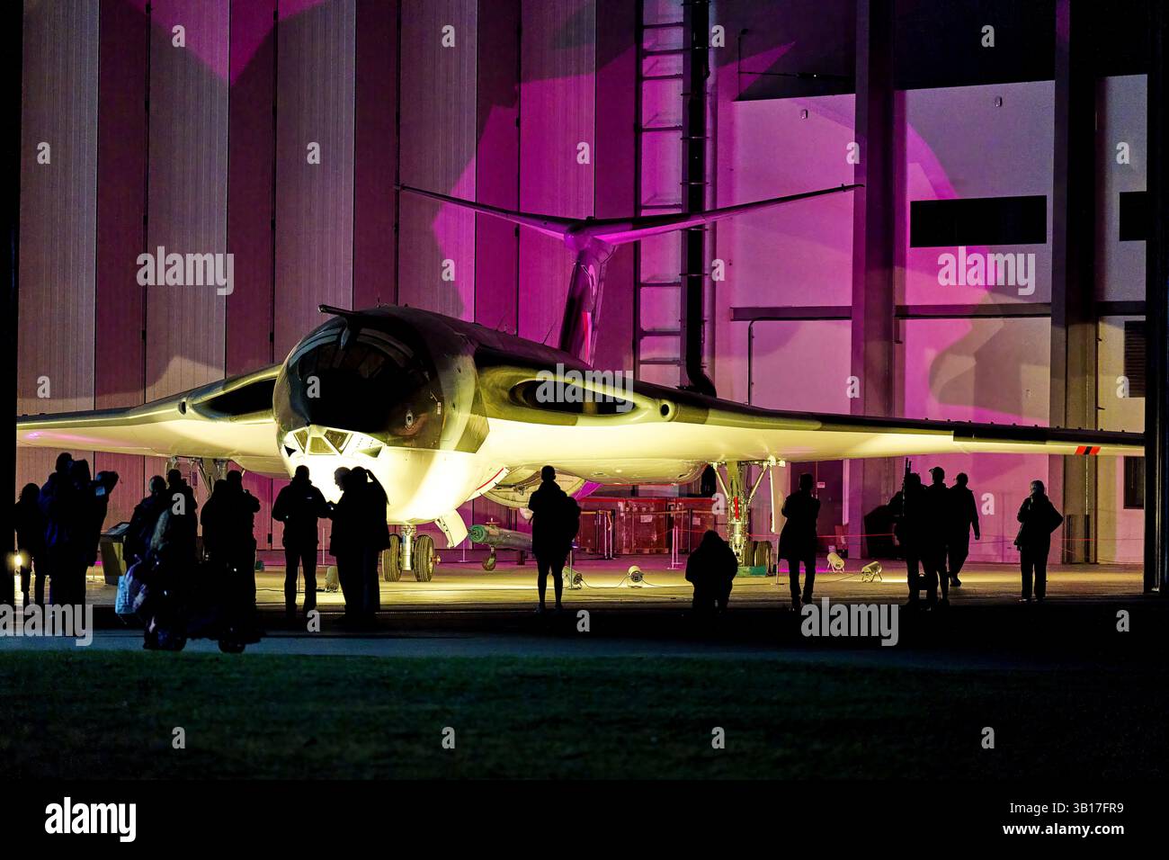 Un V-bombardiere Handley Page Victor della RAF illuminato in magenta di notte, con spettatori riuniti sotto le ali del delta a Duxford, in Inghilterra. Foto Stock