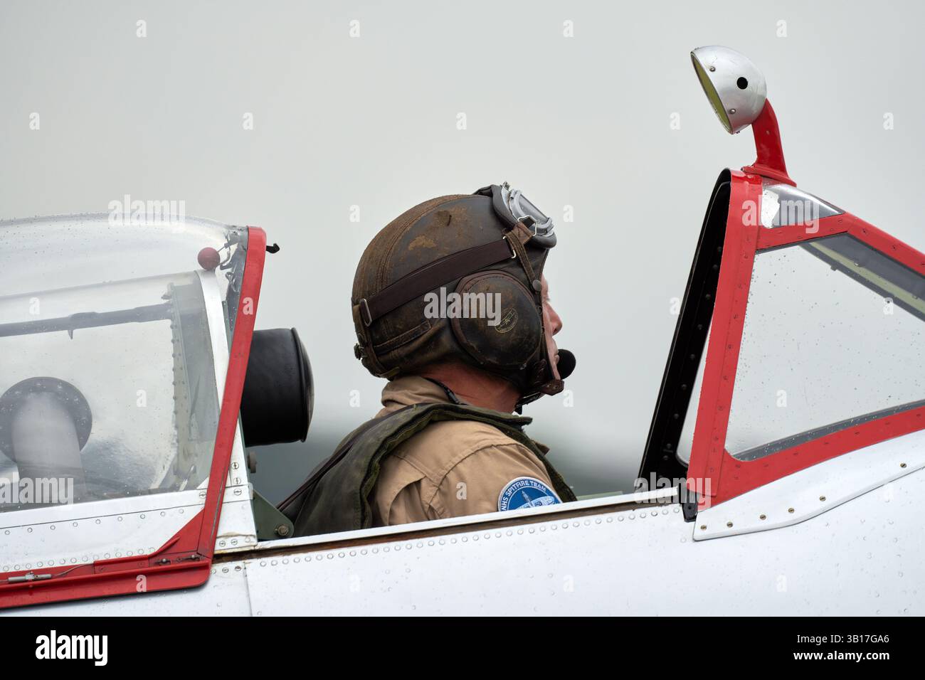 Pilota con casco e occhiali di protezione in pelle d'epoca siede nella cabina di pilotaggio di un aereo P-47 Thunderbolt, preparandosi per il volo in una giornata nuvolosa a Duxford. Foto Stock Pilota con casco e occhiali di protezione in pelle d'epoca siede nella cabina di pilotaggio di un aereo P-47 Thunderbolt, preparandosi per il volo in una giornata nuvolosa a Duxford. Foto Stock