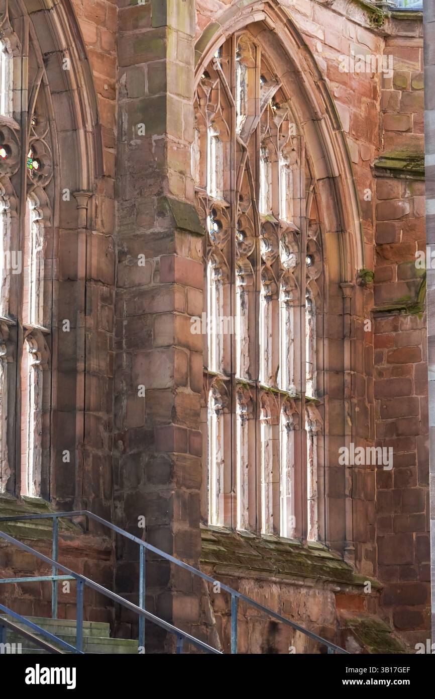 La luce del sole scorre attraverso l'intricato tracciato di una finestra gotica nelle rovine della Cattedrale di Coventry, in Inghilterra, evidenziando la resilienza del suo arco Foto Stock