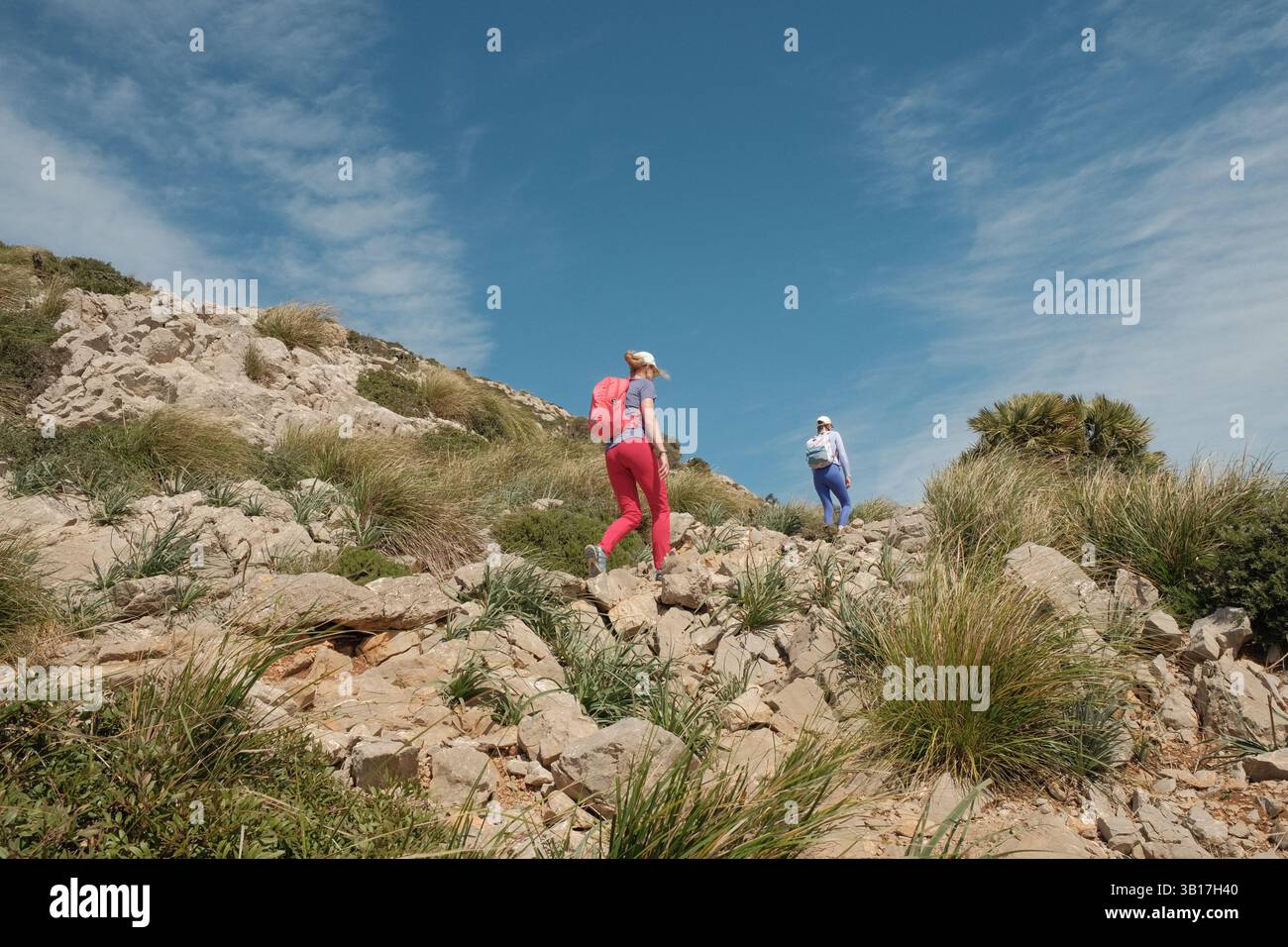 Gli escursionisti in abiti colorati arrampicano su un terreno roccioso su una collina mediterranea sotto il cielo azzurro di Maiorca. Foto Stock