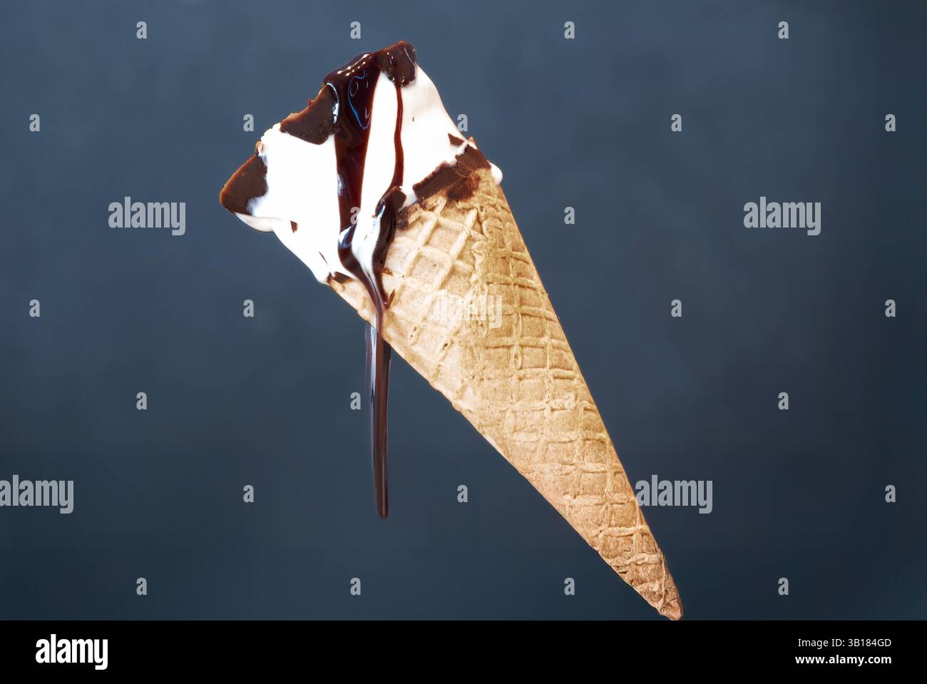Un cono gelato alla vaniglia, cosparso di sciroppo di cioccolato, si sta sciogliendo nel fuoco. Il dolce è un classico piacere estivo, Foto Stock