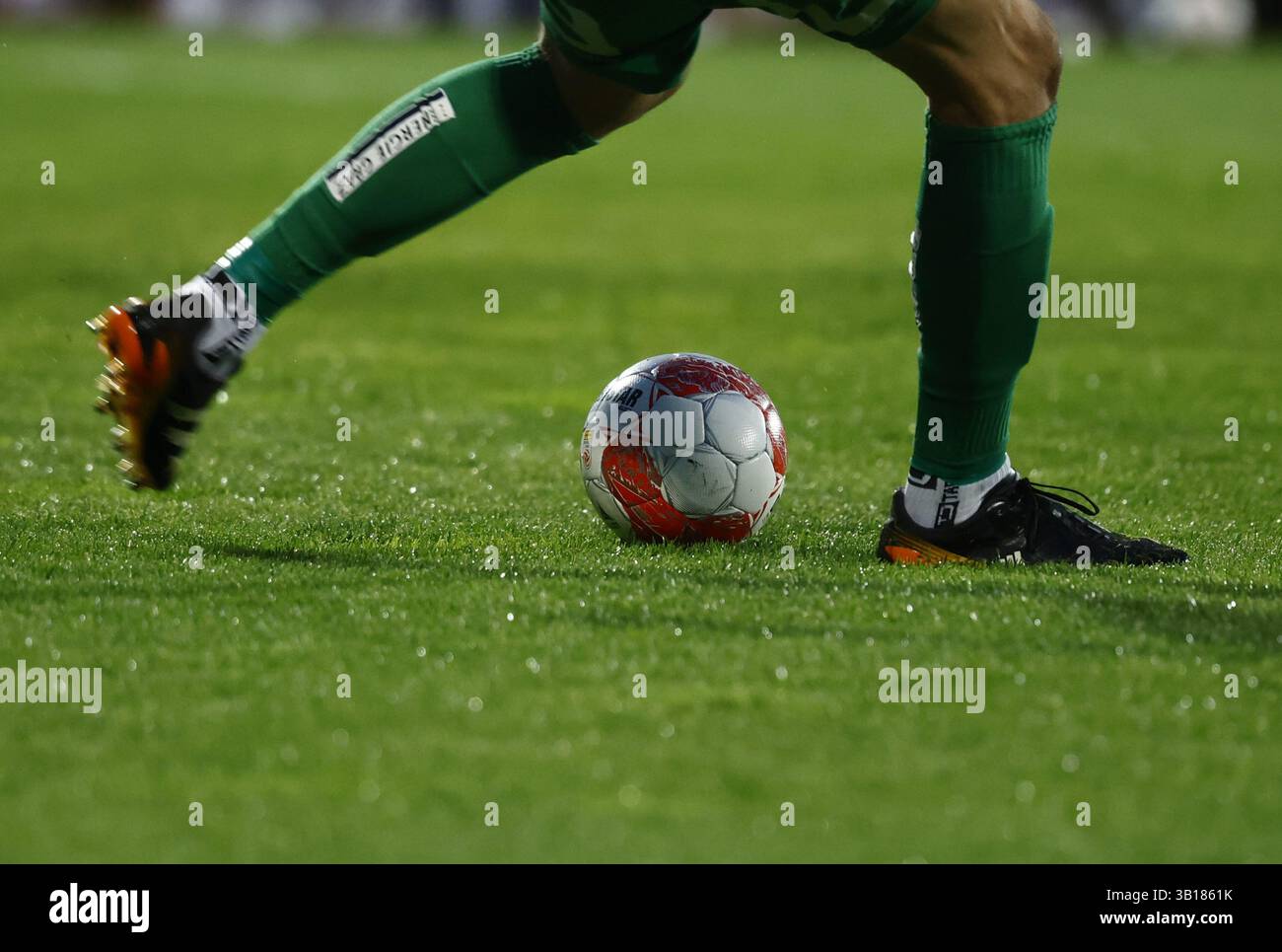 ABD0245 20250425 - HARTBERG - Österreich: THEMENBILD Illustration zu den Themen "SPORT/FUSSBALL/MANNSCHAFTSPORT". Ein Fußballer mit Grünen Stutzen schießt einen Ball vom nassen Rasen aufgenommen am Freitag, 25. Aprile 2025, ad Hartberg. - FOTO: APA/ERWIN SCHERIAU - 20250425 PD11771 credito: APA-PictureDesk/Alamy Live News Foto Stock