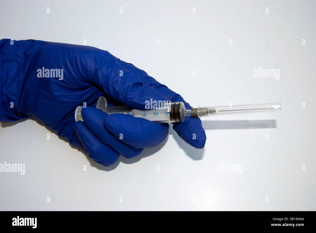 Una mano in un guanto blu con una siringa. Una mano medica che tiene una siringa monouso. La mano di un medico o di un infermiere in un guanto isolato sul bianco. Foto Stock