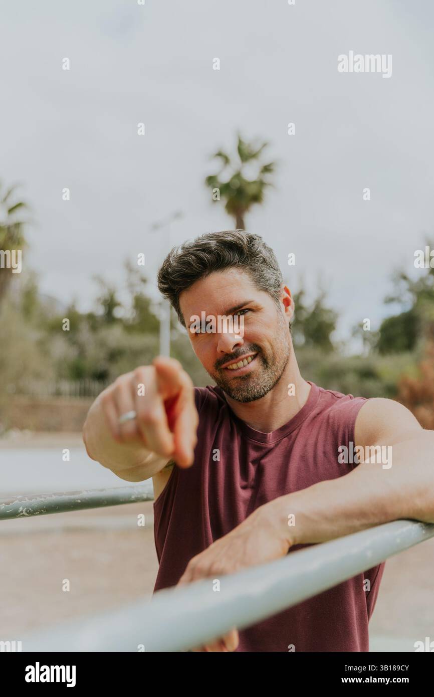 Un uomo in forma felice in una palestra all'aperto punta con il dito verso la macchina fotografica, concetto motivazionale. Foto Stock