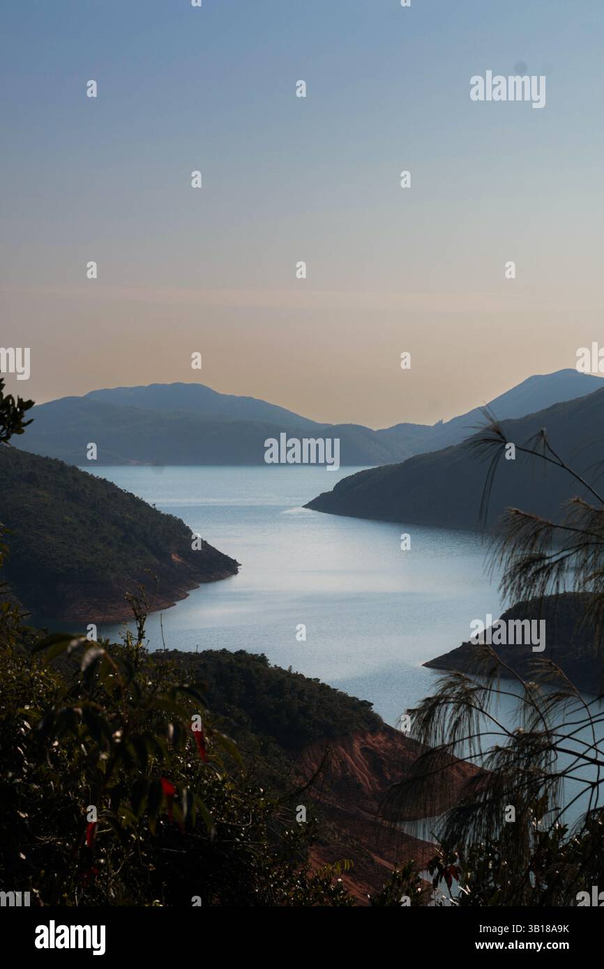 Tranquilla vista sulla natura con un vasto tratto d'acqua visto dall'alto e sagome di piccole montagne sullo sfondo sotto un cielo tranquillo. Foto Stock
