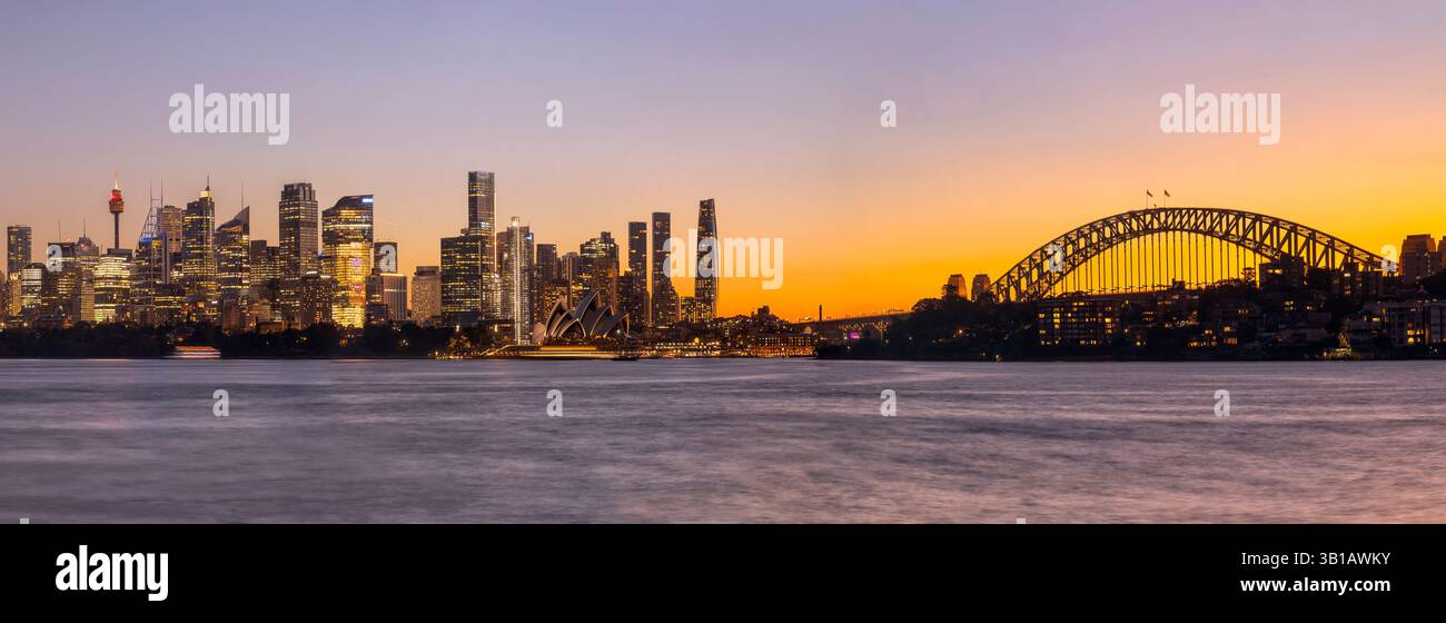 Primo piano, colorato tramonto dell'ora dorata sullo skyline del lungomare della città di Sydney in Australia, attraverso le acque del porto sfocato. Foto Stock