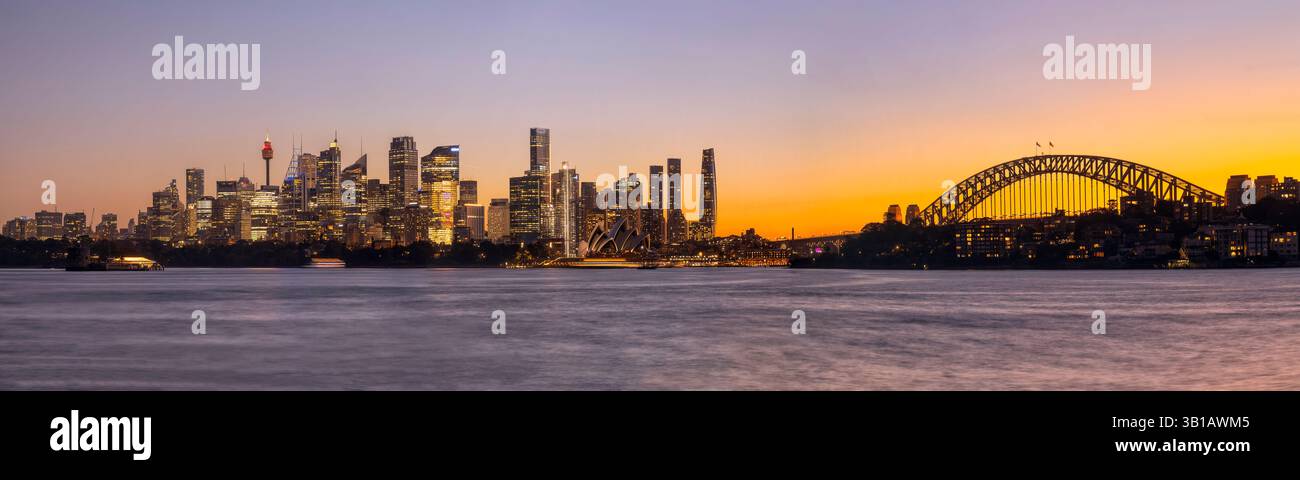 Colorato tramonto dell'ora d'oro sullo skyline del lungomare della città di Sydney in Australia attraverso le acque del porto sfocato. Foto Stock