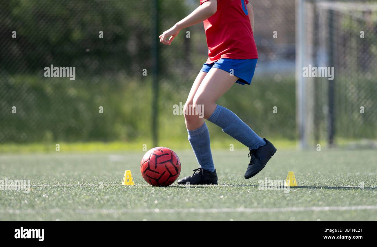 La ragazza dribbla abilmente la palla tra le Flip Cup durante le esercitazioni calcistiche, catturata in primo piano, vista laterale Foto Stock