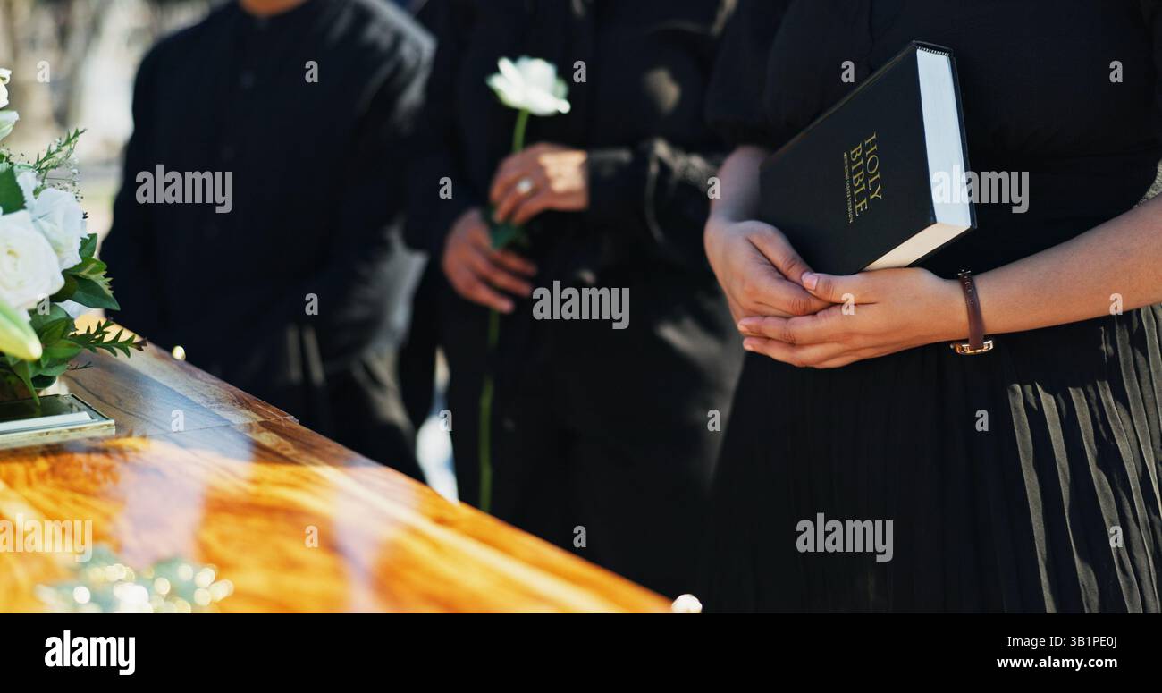 Bibbia, mani e persone per bara al funerale per rispetto, benedizione o conforto spirituale al cimitero. Religione, preghiera e famiglia per scrigno con sacro Foto Stock