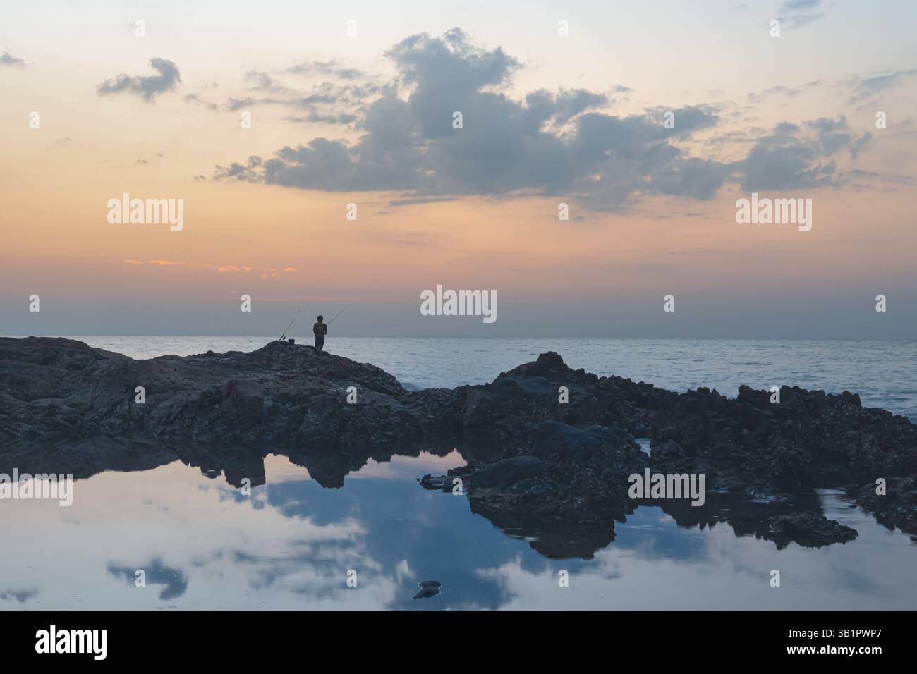 Seascape in Thailandia kaolak. Cresta costiero rocciosa sullo sfondo del tramonto, panorama. Una piccola silhouette di un pescatore sulle rocce Foto Stock