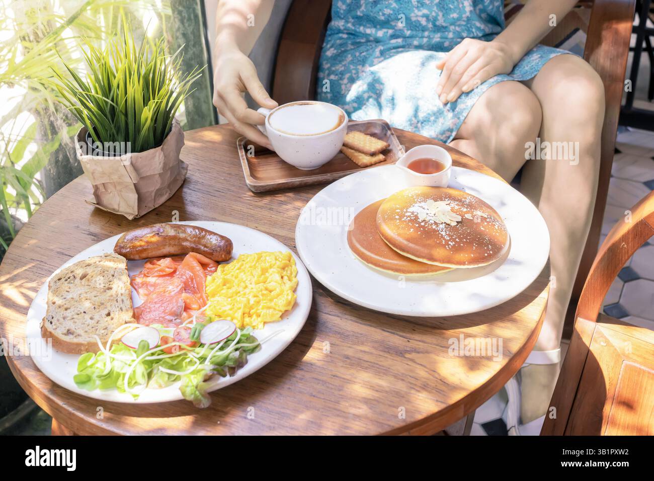 Una deliziosa colazione e' organizzata su un tavolo di legno in un affascinante Cafe'. Il pasto consiste in soffici pancake conditi con sciroppo, uova strapazzate, cri Foto Stock