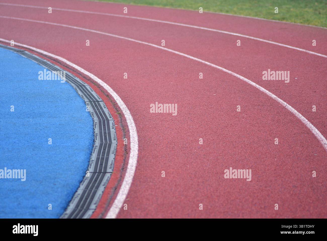 curva rossa della pista da corsa con linee bianche, campo sportivo blu sul lato sinistro e erba verde sul lato destro Foto Stock