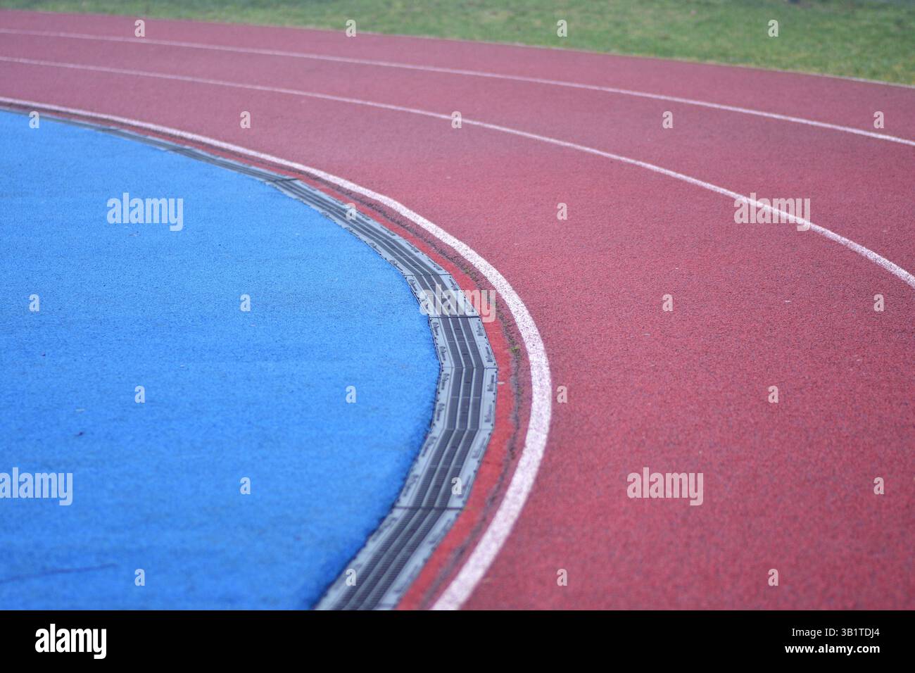 curva rossa della pista da corsa con linee bianche, campo sportivo blu sul lato sinistro e erba verde sul lato destro Foto Stock