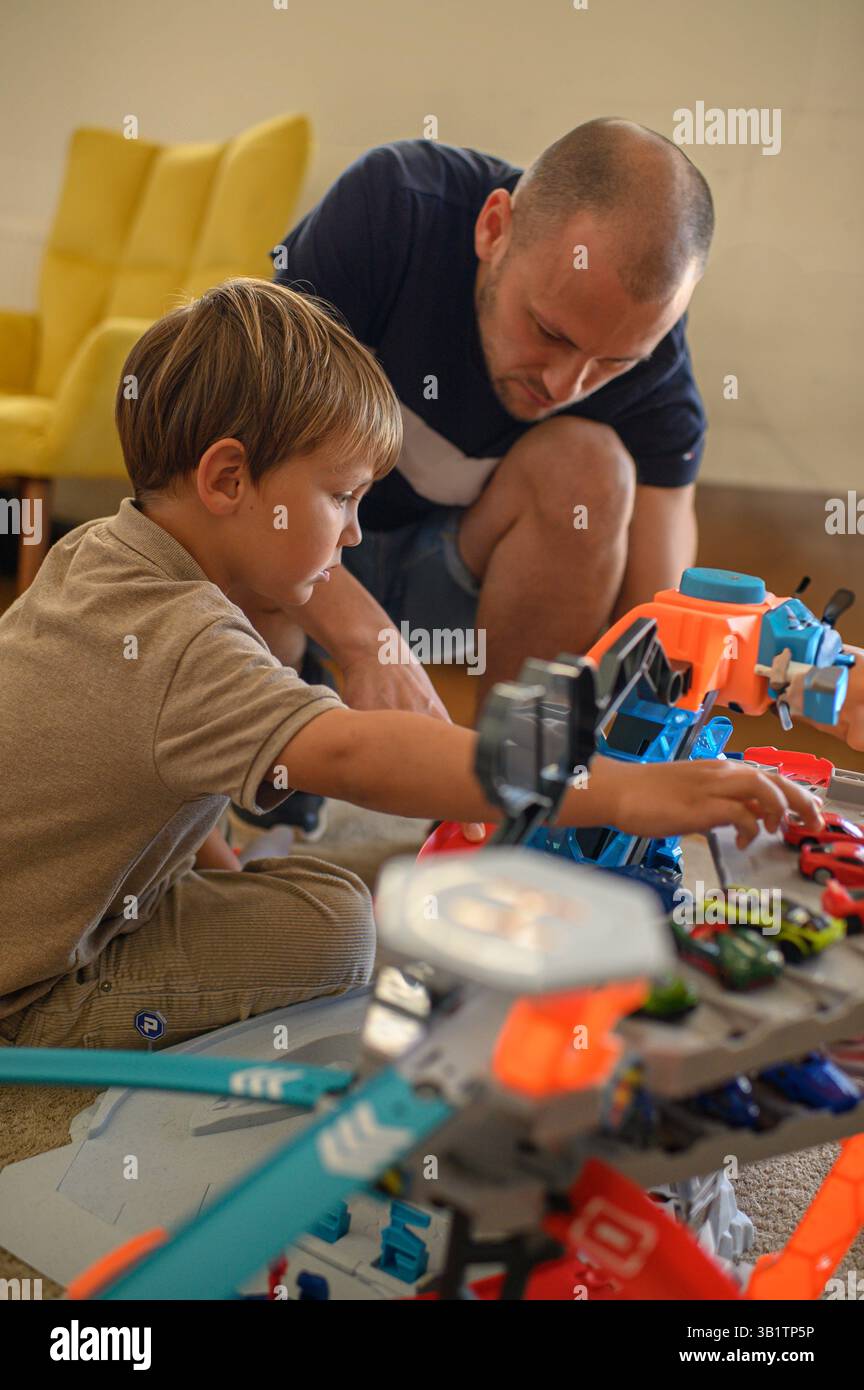 Padre e figlio giocano con il circuito a casa. Momenti di legame felice, emozioni per l'infanzia e tempo per la famiglia con le auto giocattolo in un'atmosfera accogliente Foto Stock