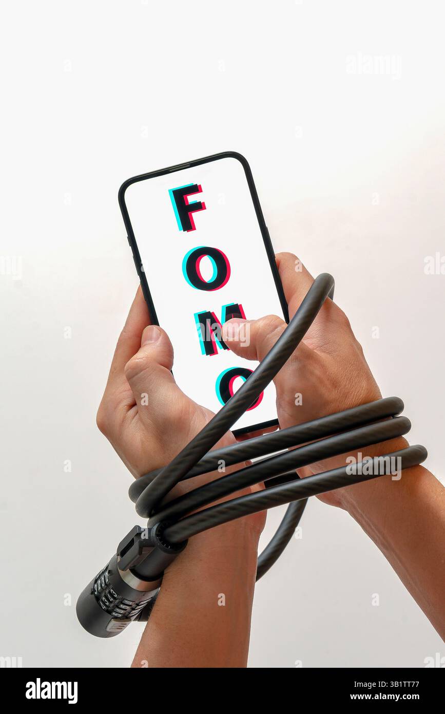 Le mani sono bloccate con un blocco cavo, tenendo in mano uno smartphone con FOMO (paura di perdere): Dipendenza dai social media, paura di perdere notizie Foto Stock