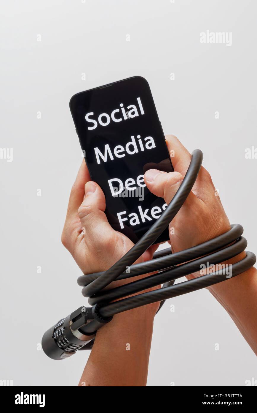 Le mani sono bloccate con un blocco del cavo, tenendo in mano uno smartphone con la scritta Social Media Deep Fakes, paura di perdere importanti aggiornamenti Foto Stock